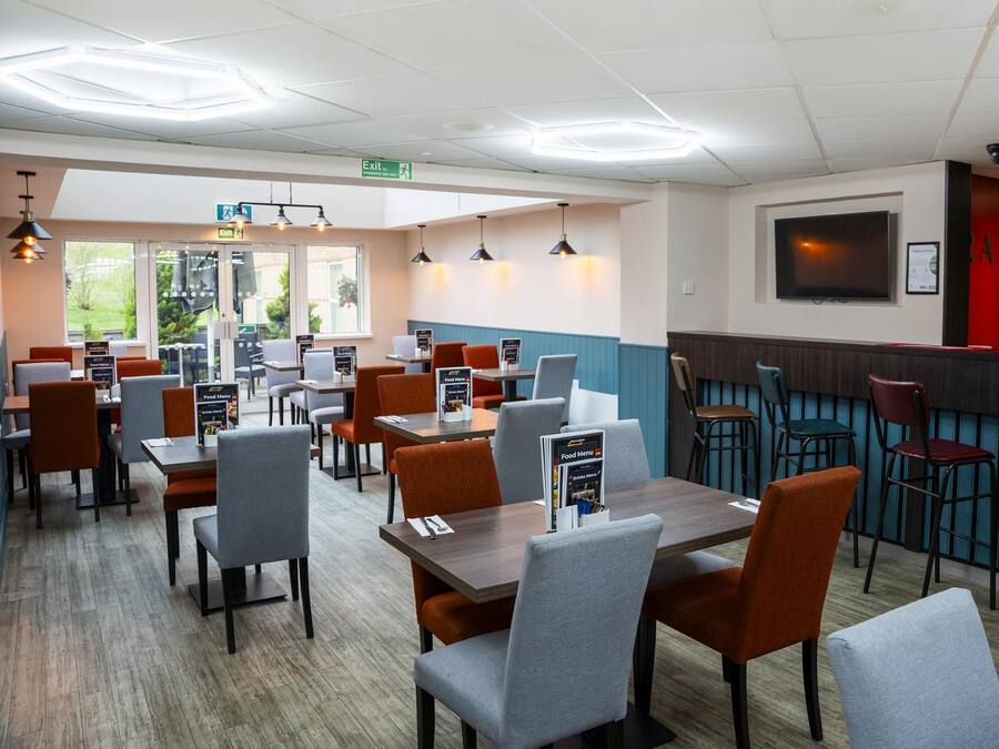 A restaurant with multiple tables and chairs, a counter area, and a TV mounted on the wall.