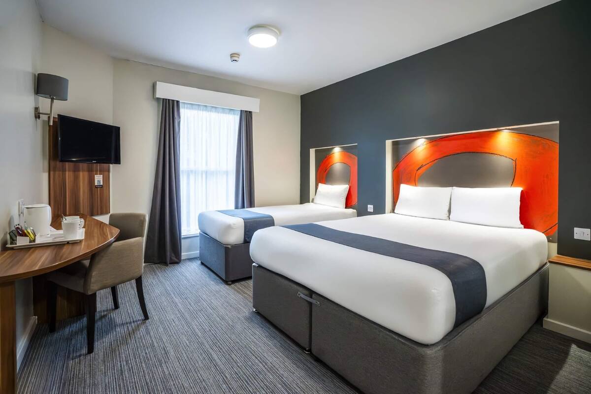 A hotel room with a large bed, a desk with a chair, a TV, and a window with curtains.