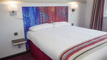 A hotel room with a bed, a nightstand, a wall-mounted lamp, and a colorful abstract painting above the bed.