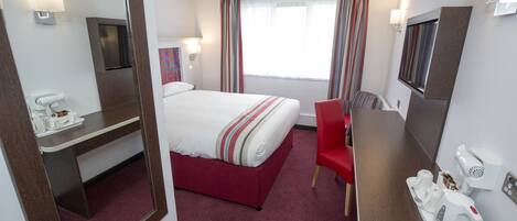 Habitación de hotel con cama, escritorio, silla, espejo, televisor y ventana con cortinas.