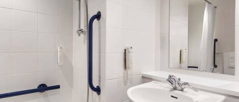 Un baño moderno con azulejos blancos, un lavabo blanco, un espejo y una ducha con cabezal de ducha manual.