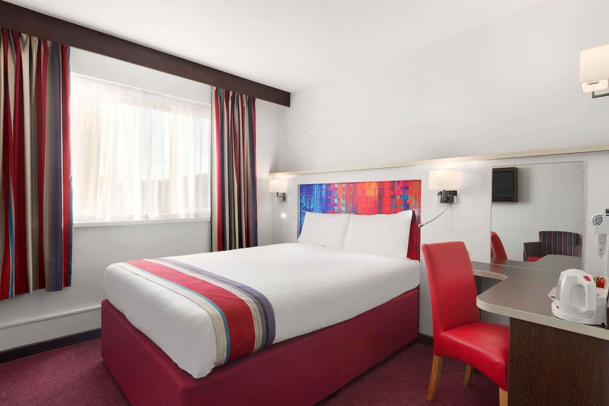 Ein Hotelzimmer mit einem Bett, einem Schreibtisch mit Stuhl, einem Fernseher und einem Fenster mit Vorhängen.