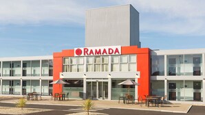 Un edificio moderno con una fachada destacada de rojo y blanco, que muestra el nombre 'RAMADA' y numerosas ventanas de vidrio.