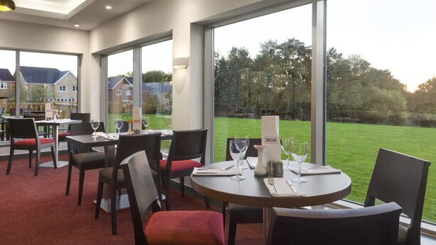Un restaurante con mesas redondas, sillas y vistas a un área con césped y casas.