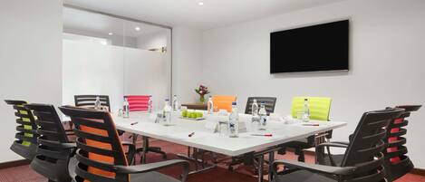 A conference room with a white table, black and orange chairs, a flat-screen TV, and a mirror on the wall.