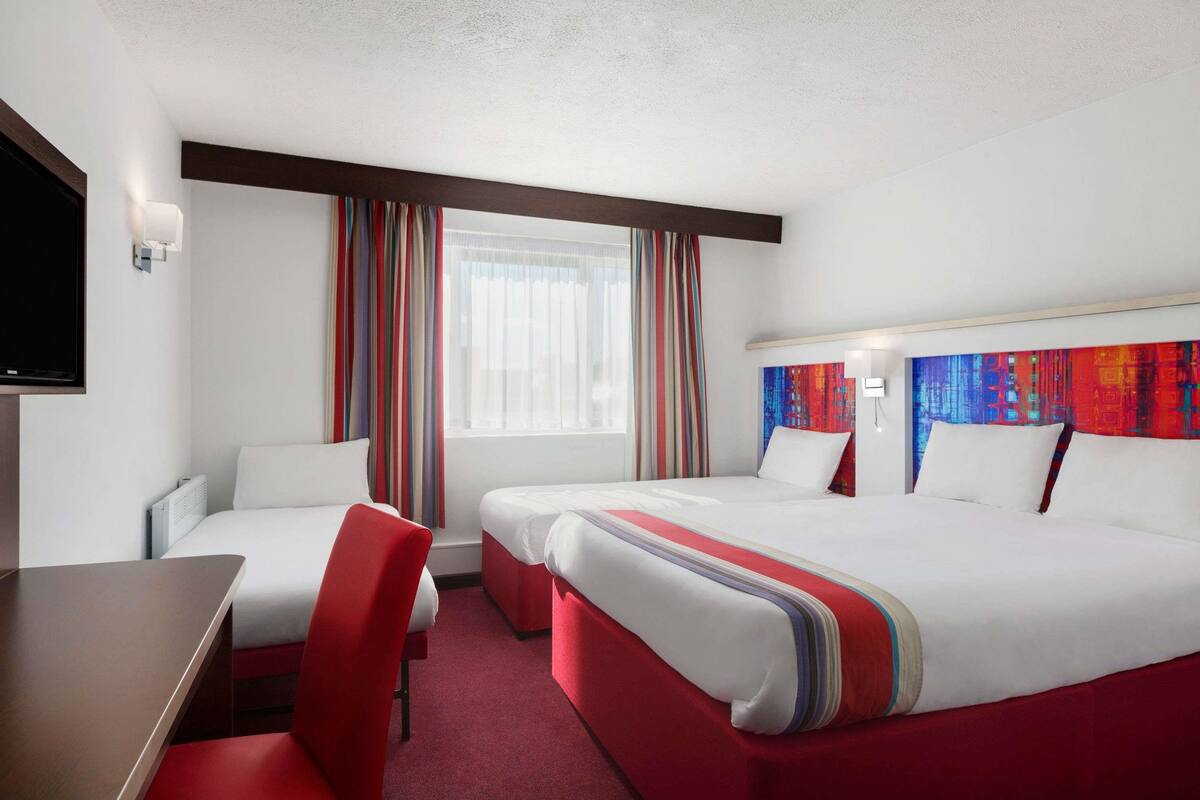 Ein Hotelzimmer mit zwei Betten, einem Schreibtisch und einem Fernseher.