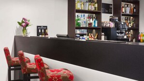 Una zona de bar con mostrador, estantes llenos de botellas de licor y dos sillas con tapicería floral.