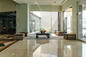 Un vestíbulo moderno con entrada por puerta de vidrio, una mesa de centro y zonas de estar.