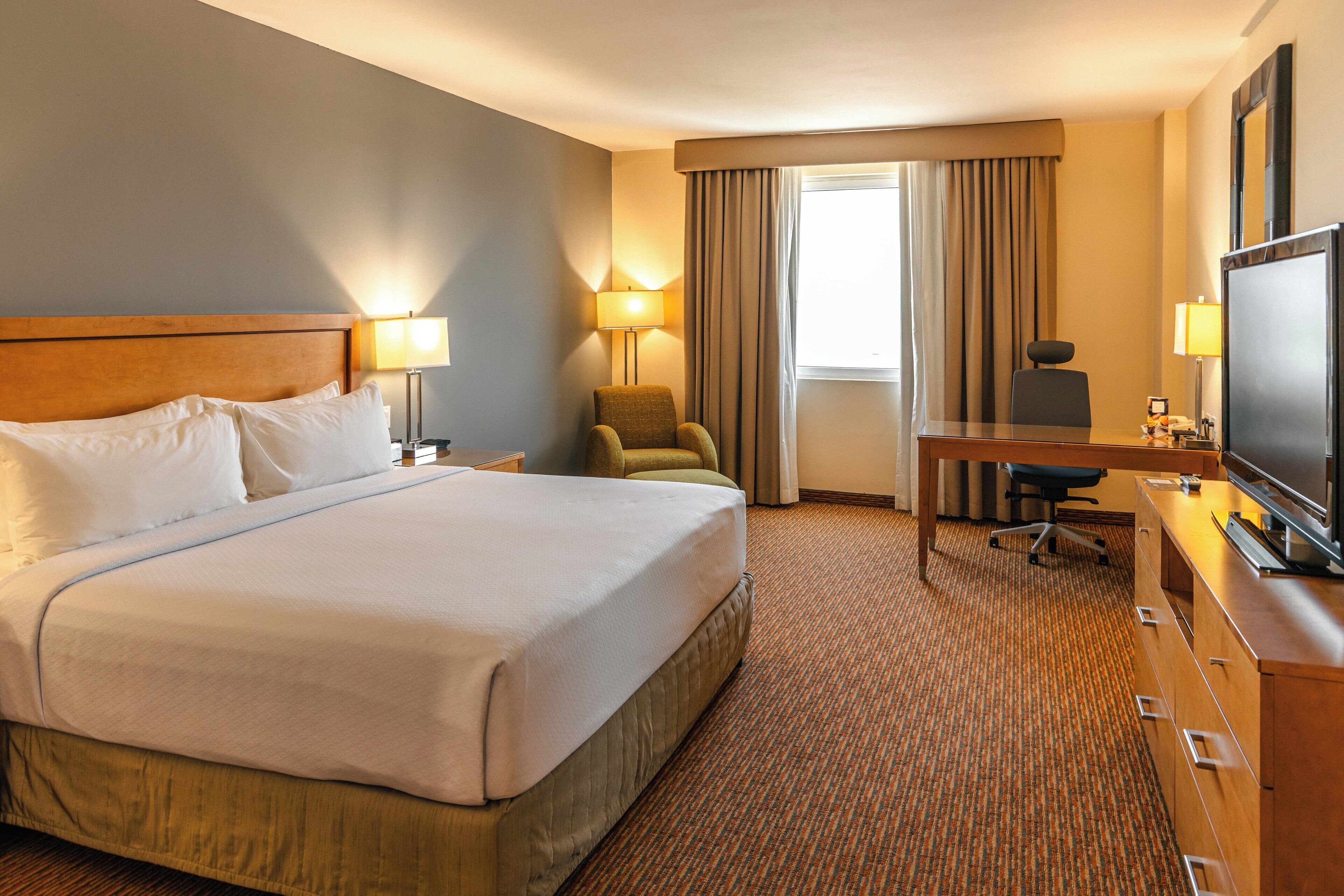 Une chambre d’hôtel avec un grand lit, un bureau, une chaise, une télévision et une lampe.