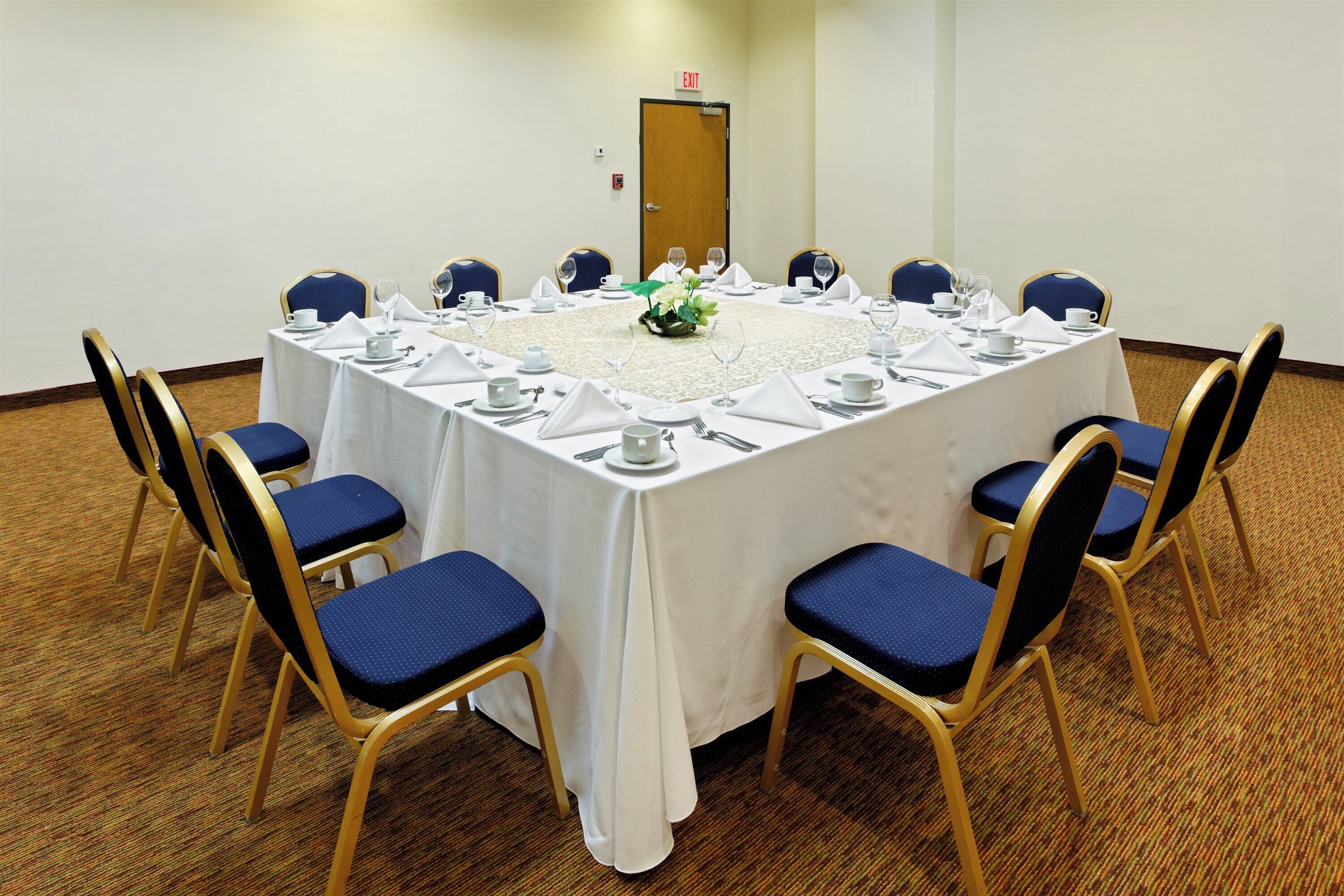 Un salón de conferencias con una mesa redonda, sillas y una puerta con letrero de salida.