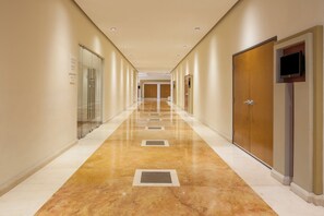 A hotel corridor with a polished floor, doors on both sides, and a sign indicating a business center.