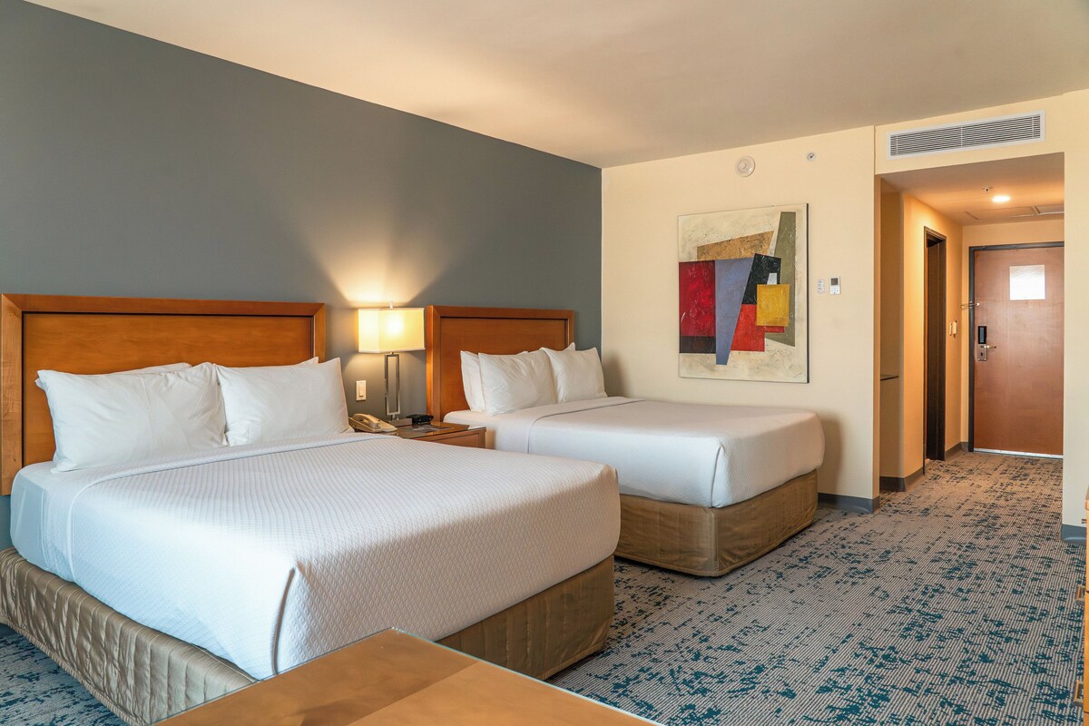 Une chambre d’hôtel avec deux lits, une table de chevet, une lampe, un tableau au mur et une porte.