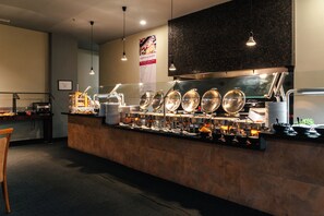 Montaje tipo buffet con varias estaciones de servicio, una barra y una zona de estar con una silla.