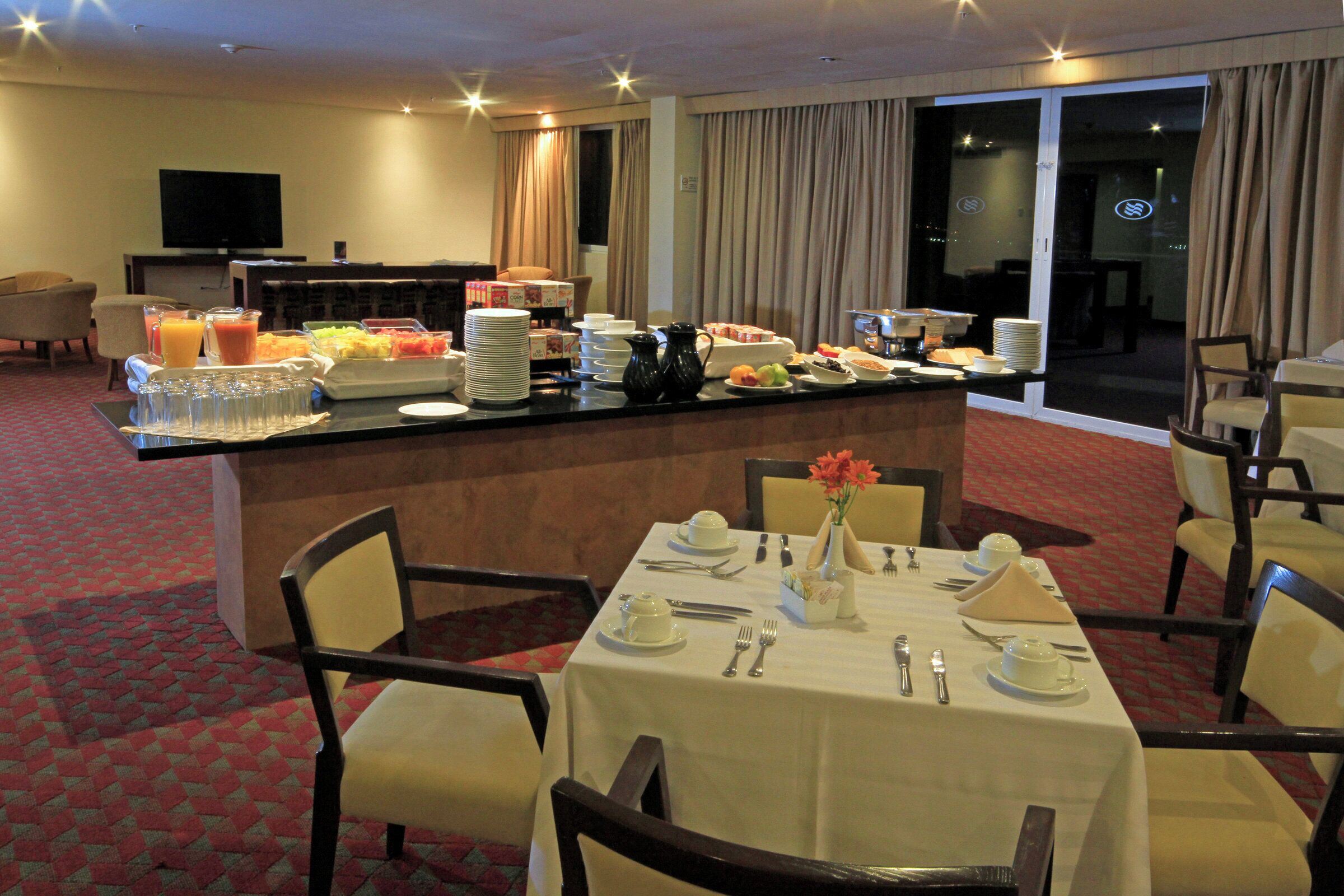 Een restaurantgedeelte in een hotel met een buffet, eettafels gedekt met bestek, en een televisie op de achtergrond.