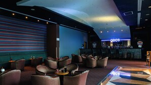 Eine Bar mit einer Neonreklame, Sitzgelegenheiten an Tischen und einem gemusterten Boden.
