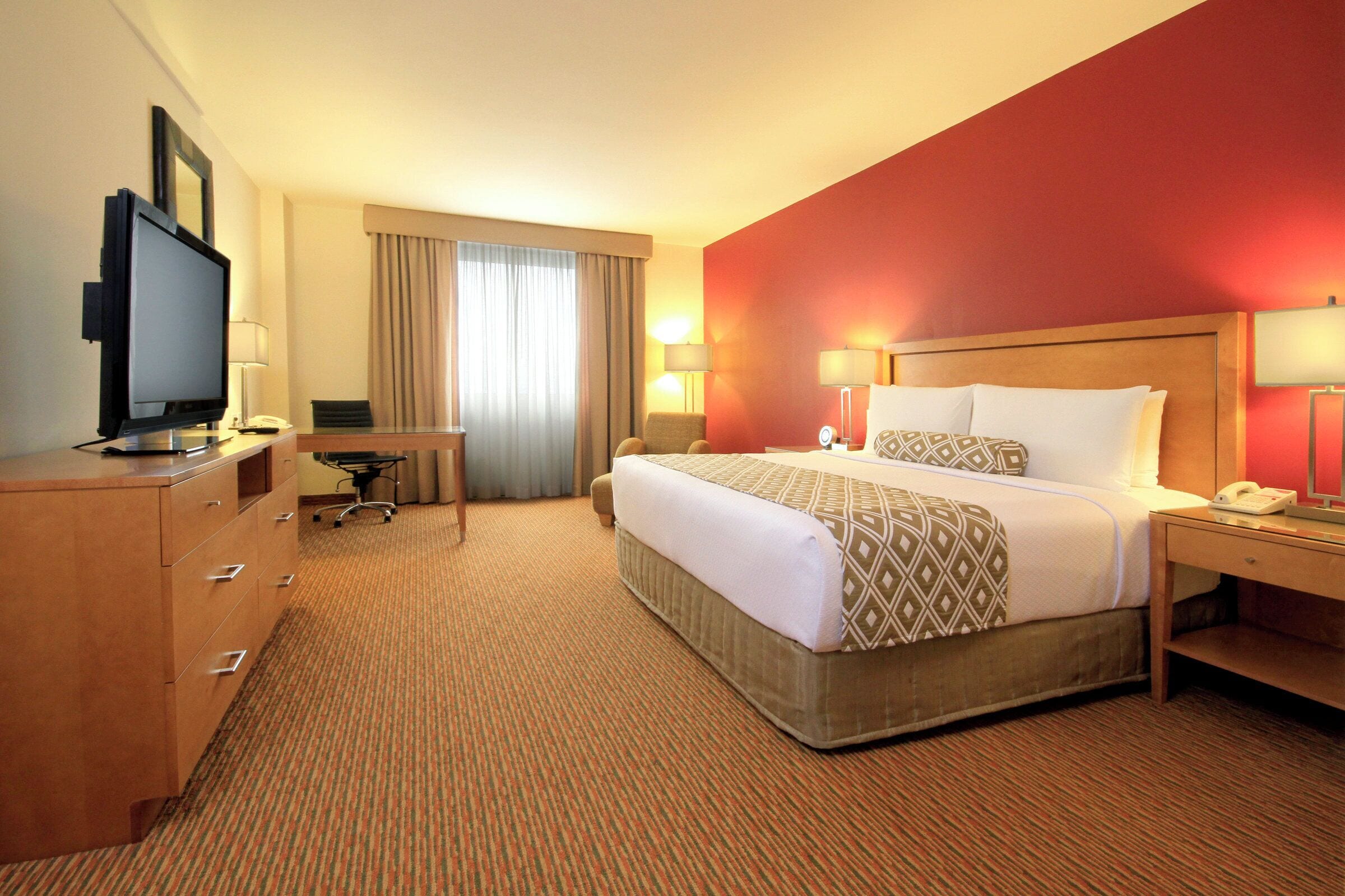 Habitación de hotel con cama, escritorio, televisión y lámparas.