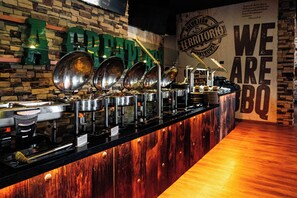 Een buffetopstelling met meerdere aanzitpunten, een bakstenen muur en een bord waarop staat 'We Are BBQ'.