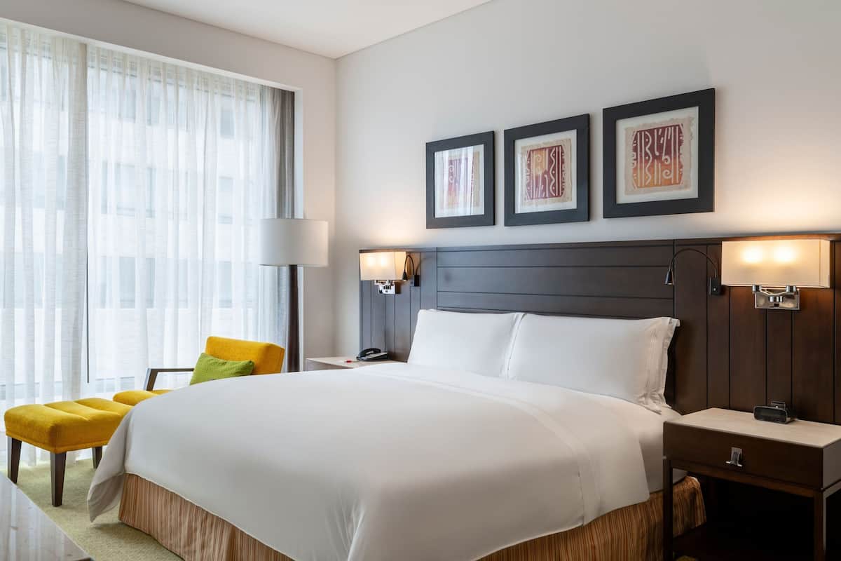 A hotel room with a large bed, bedside lamps, a nightstand, and a chair.