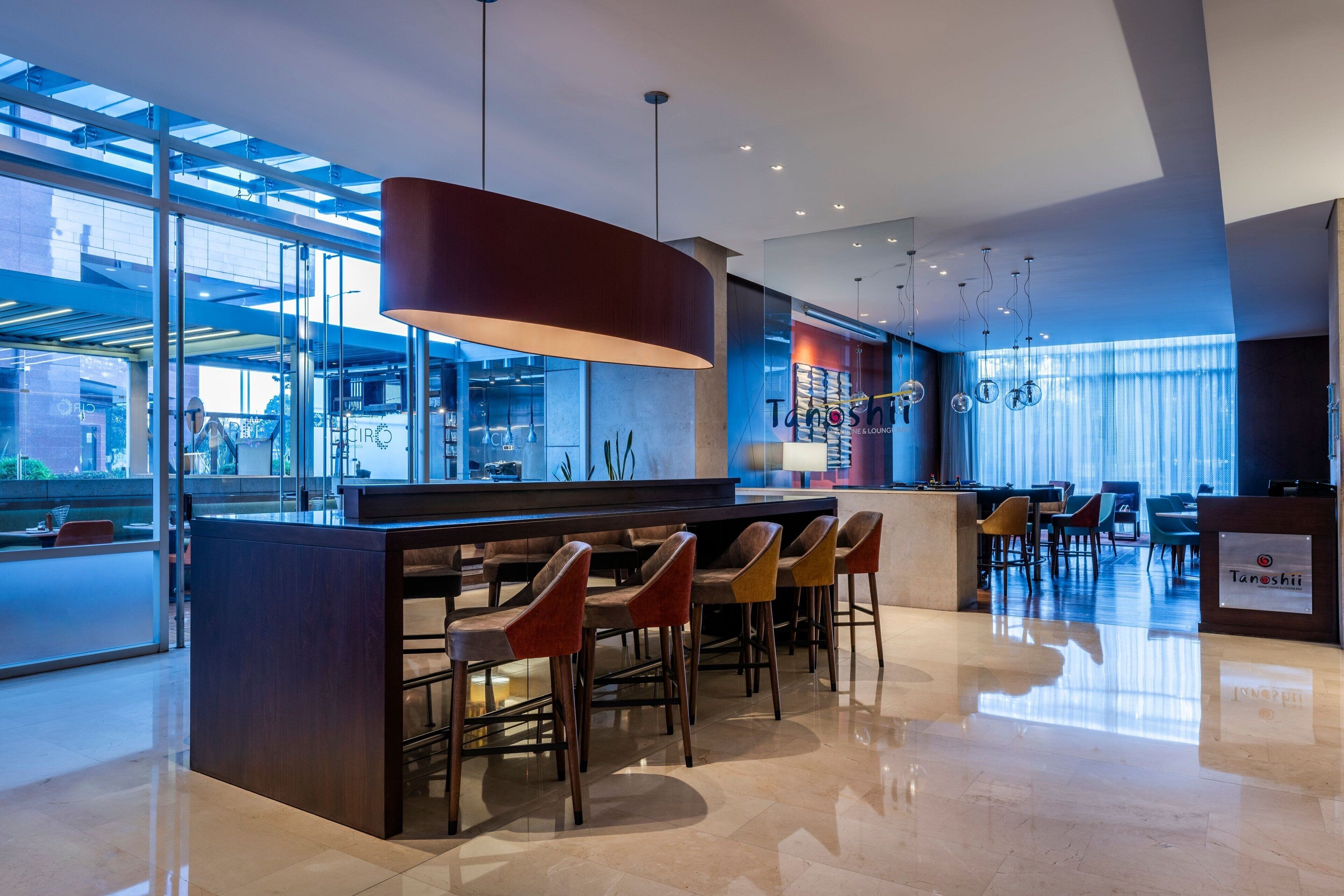 A modern bar area with a central island and multiple stools, large windows, and a clean, reflective floor.