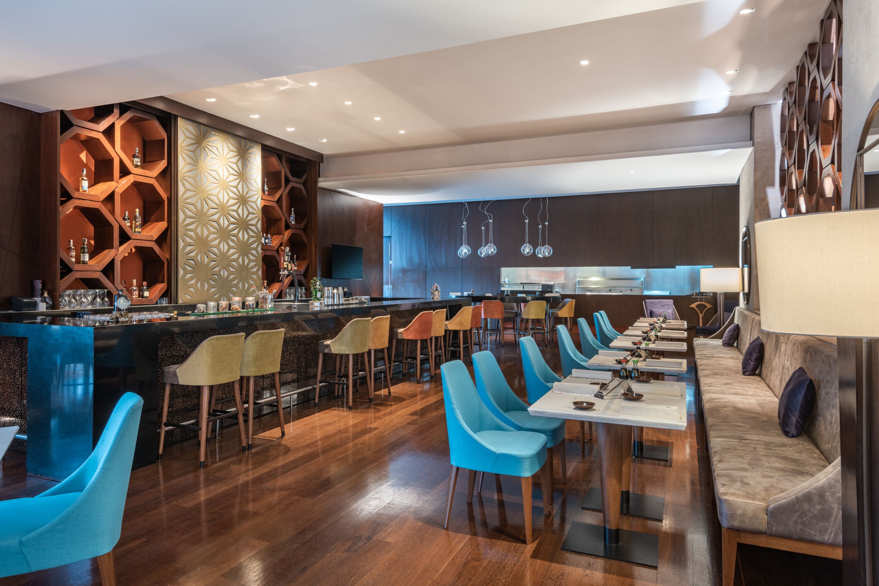 A modern bar area with a long counter, multiple seating options including bar stools and cushioned chairs, and a patterned wall design.