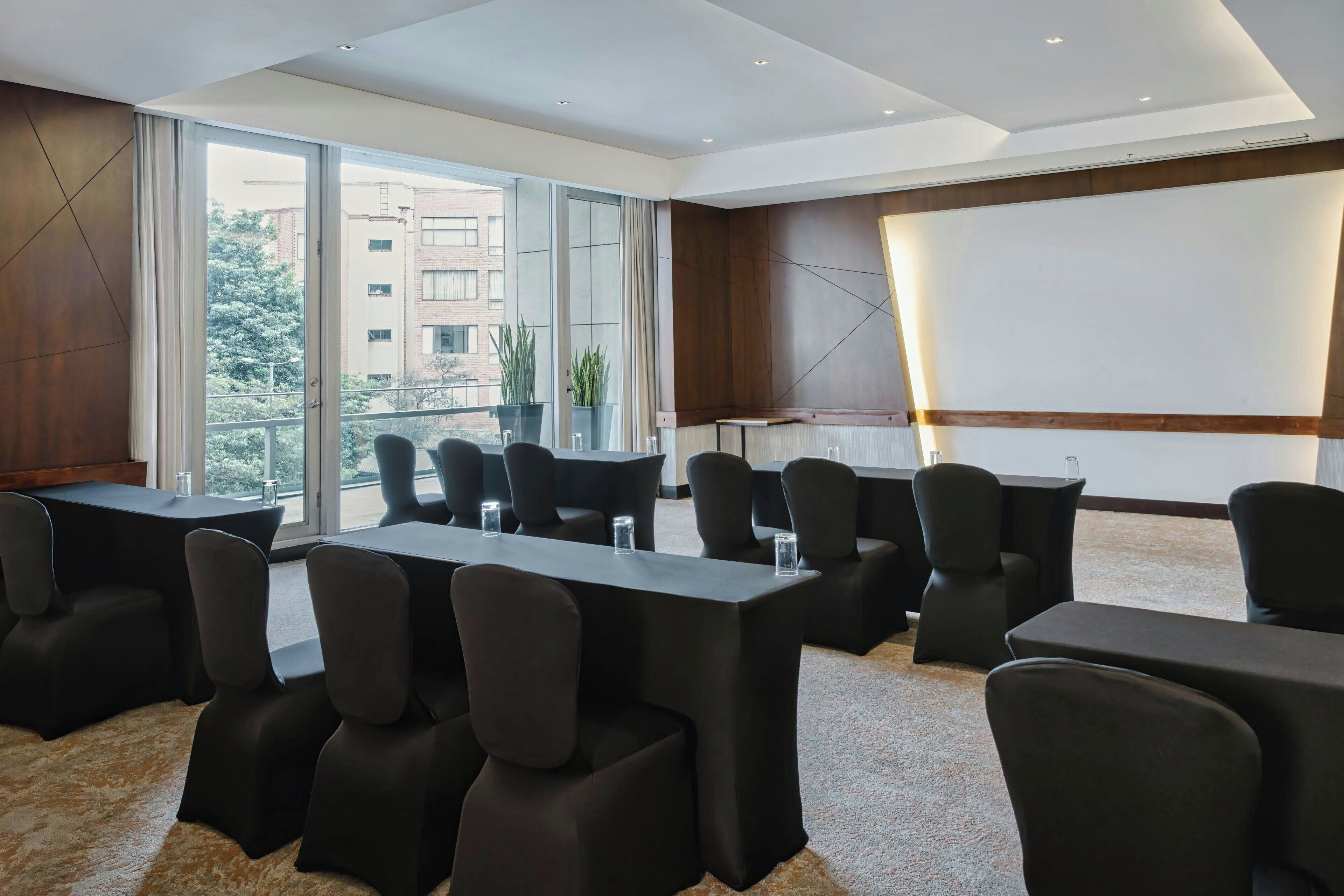 A conference room with tables and chairs, large windows, and a projector screen.