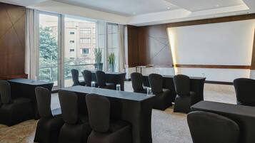 A conference room with tables and chairs, large windows, and a projector screen.