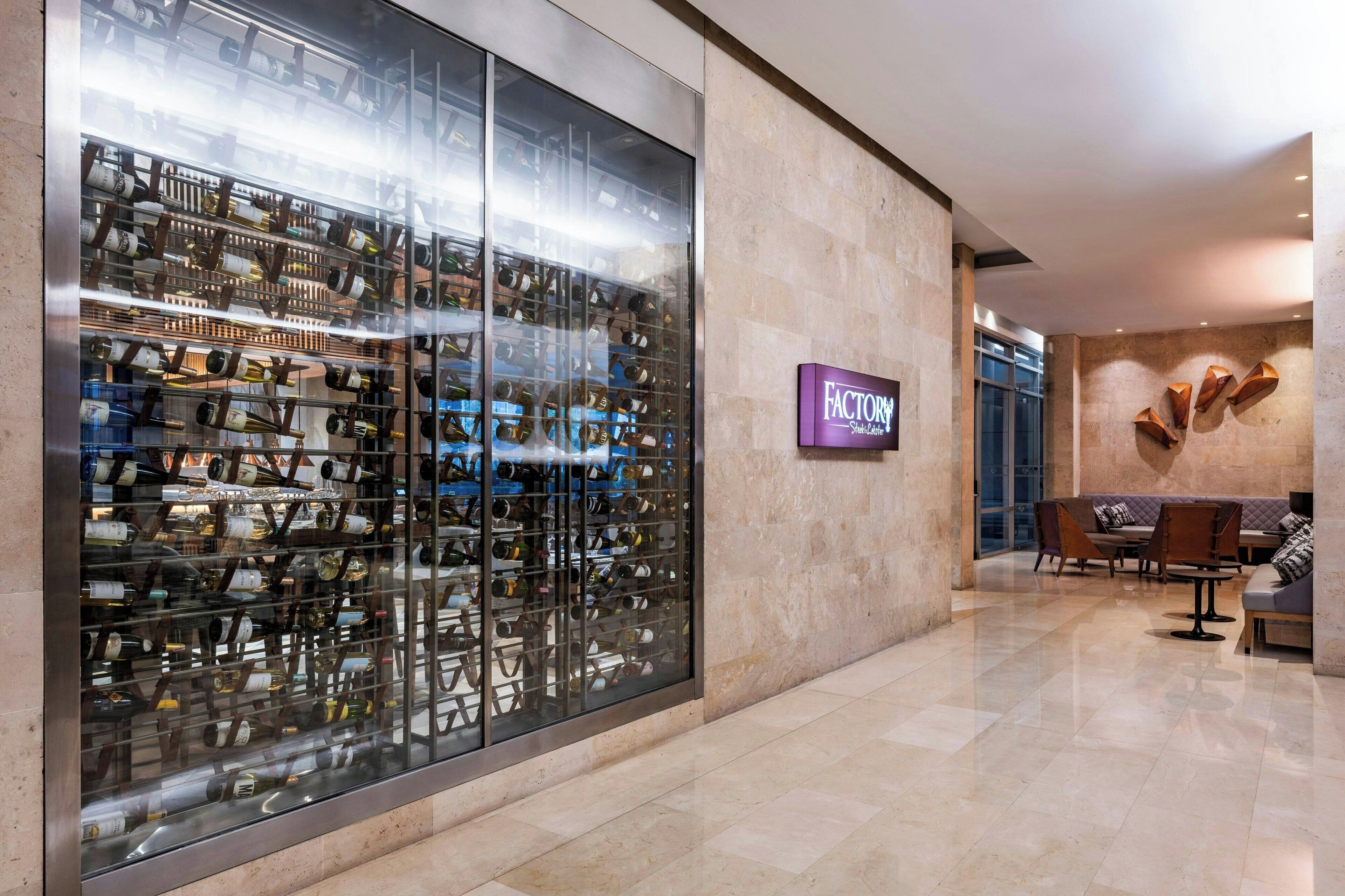 A modern hotel lobby with a wine cellar display, a seating area, and a sign for 'FACTORY'.