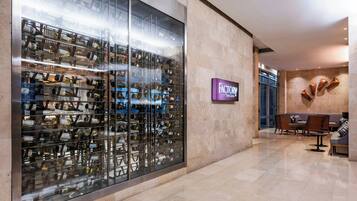 A modern hotel lobby with a wine cellar display, a seating area, and a sign for 'FACTORY'.