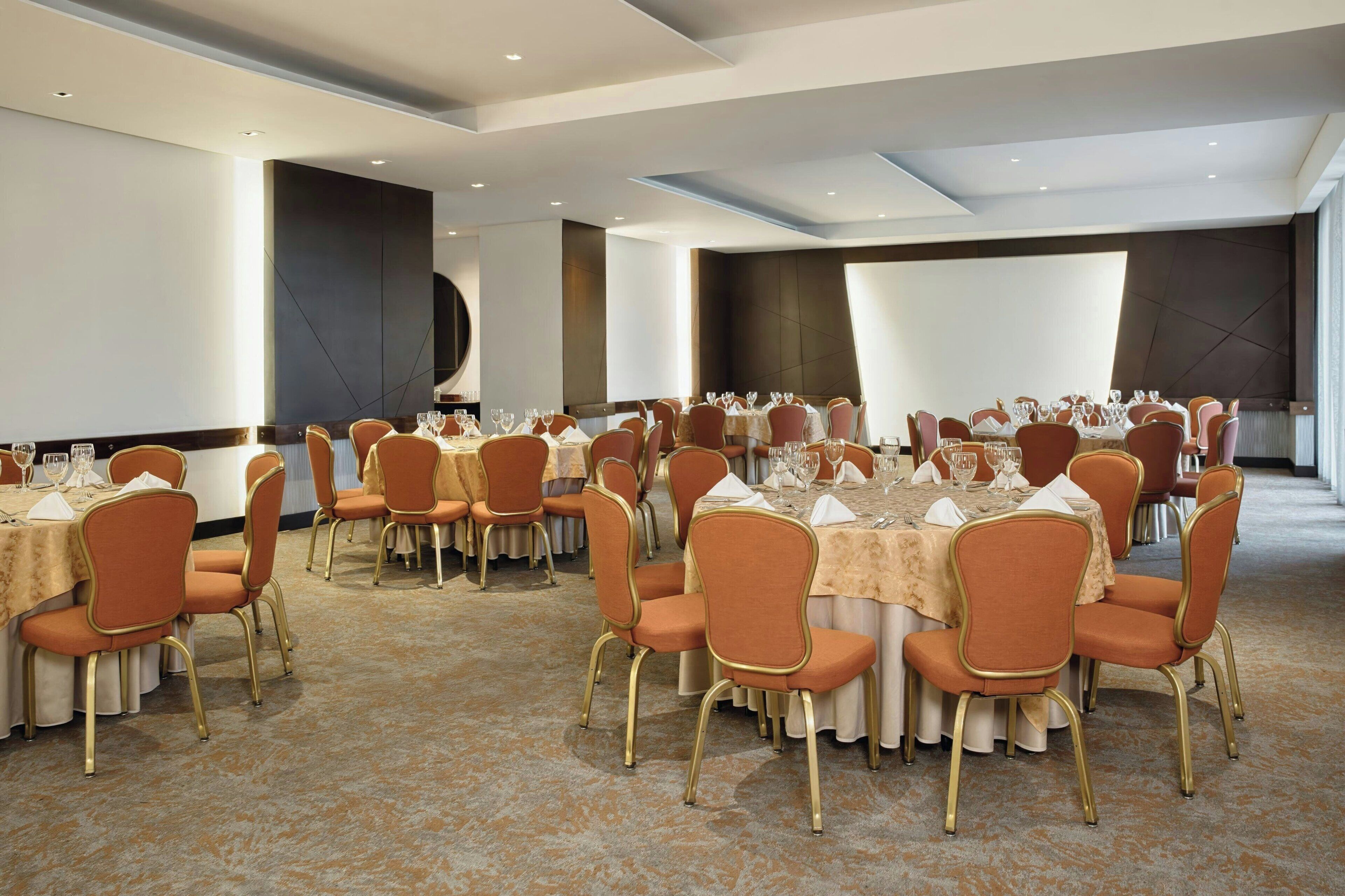A conference room with round tables, orange upholstered chairs, and a carpeted floor.