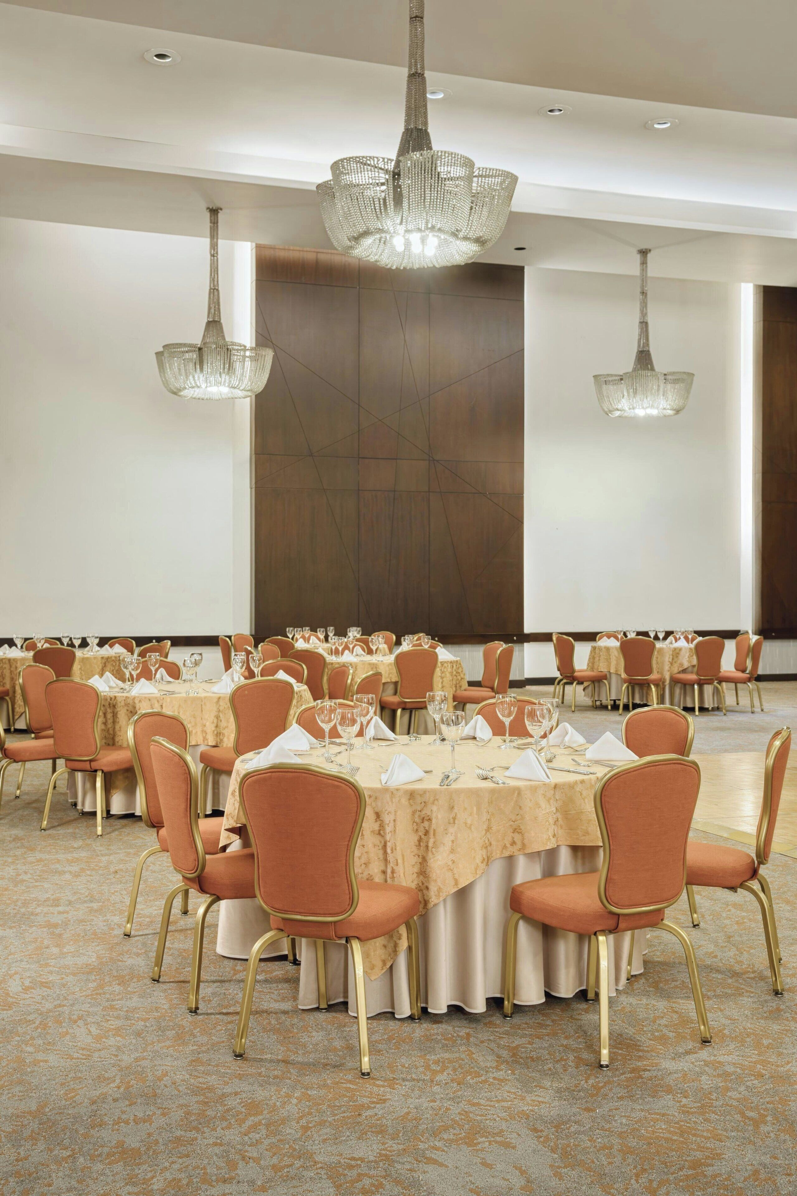 A banquet hall with round tables, chairs, and chandeliers.