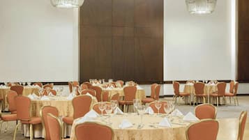 A banquet hall with round tables, chairs, and chandeliers.