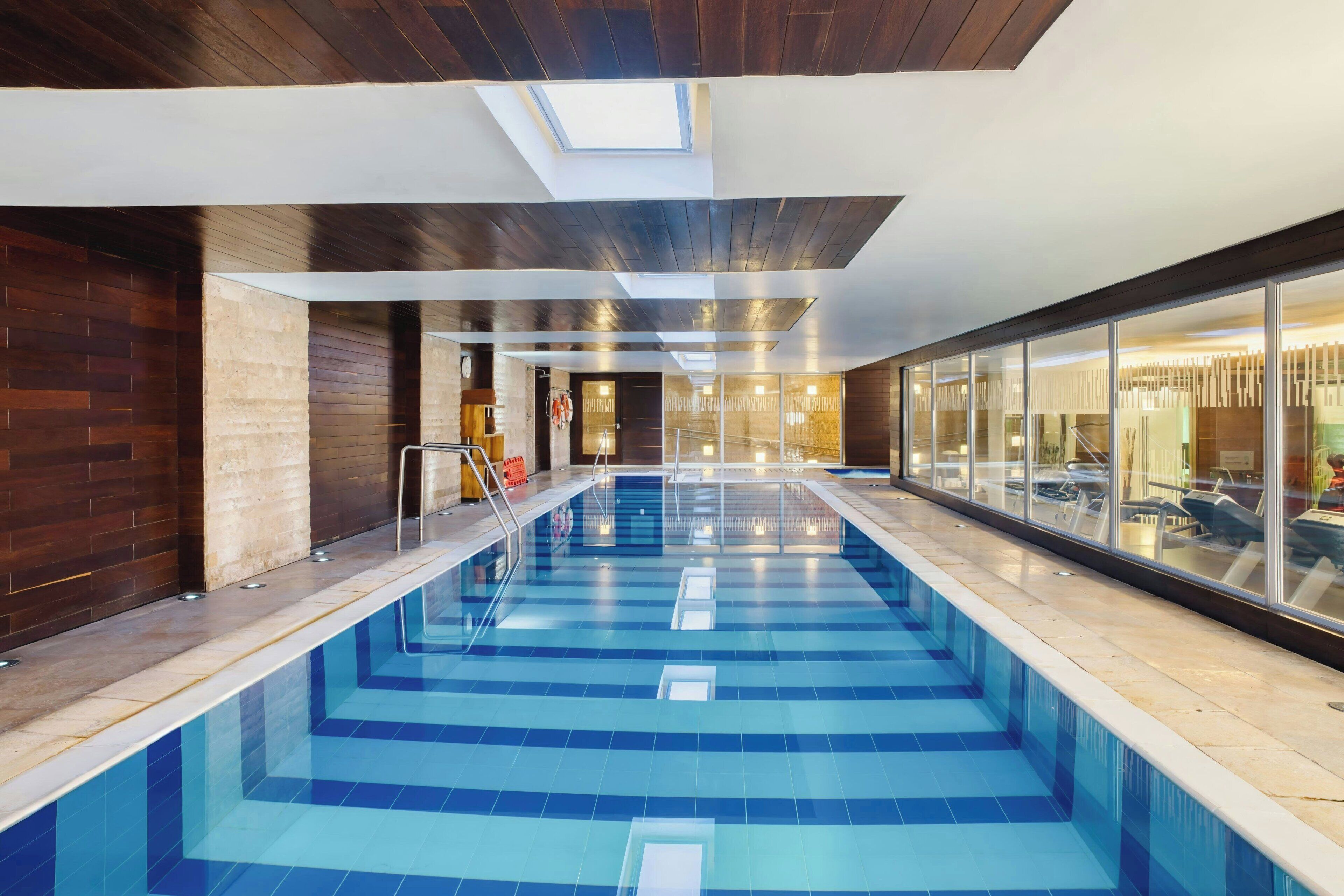 Una piscina interior con tragaluces, paredes de madera y vistas a un área de spa.