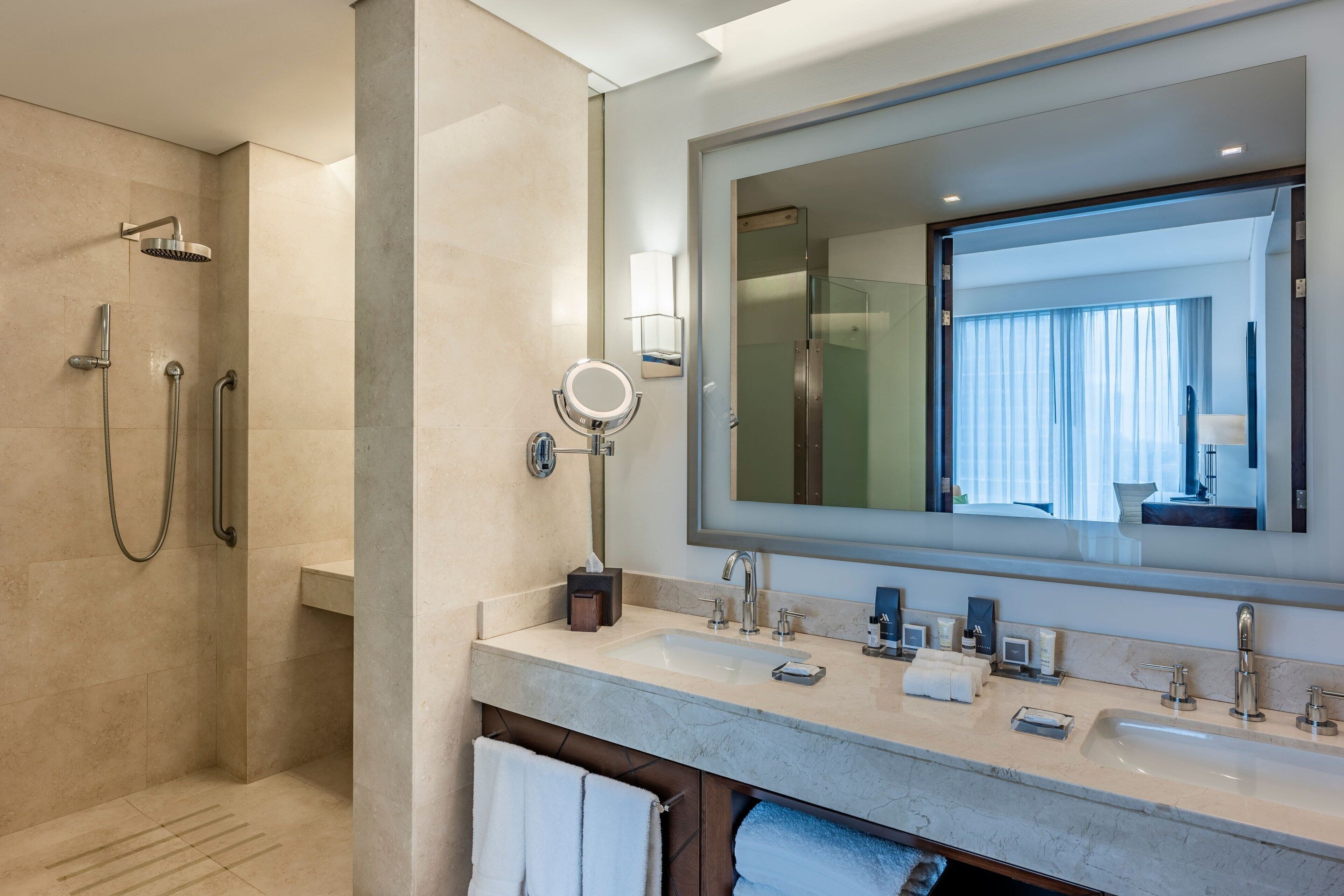 A modern bathroom with a large mirror, dual sinks, a shower area, and a towel rack.