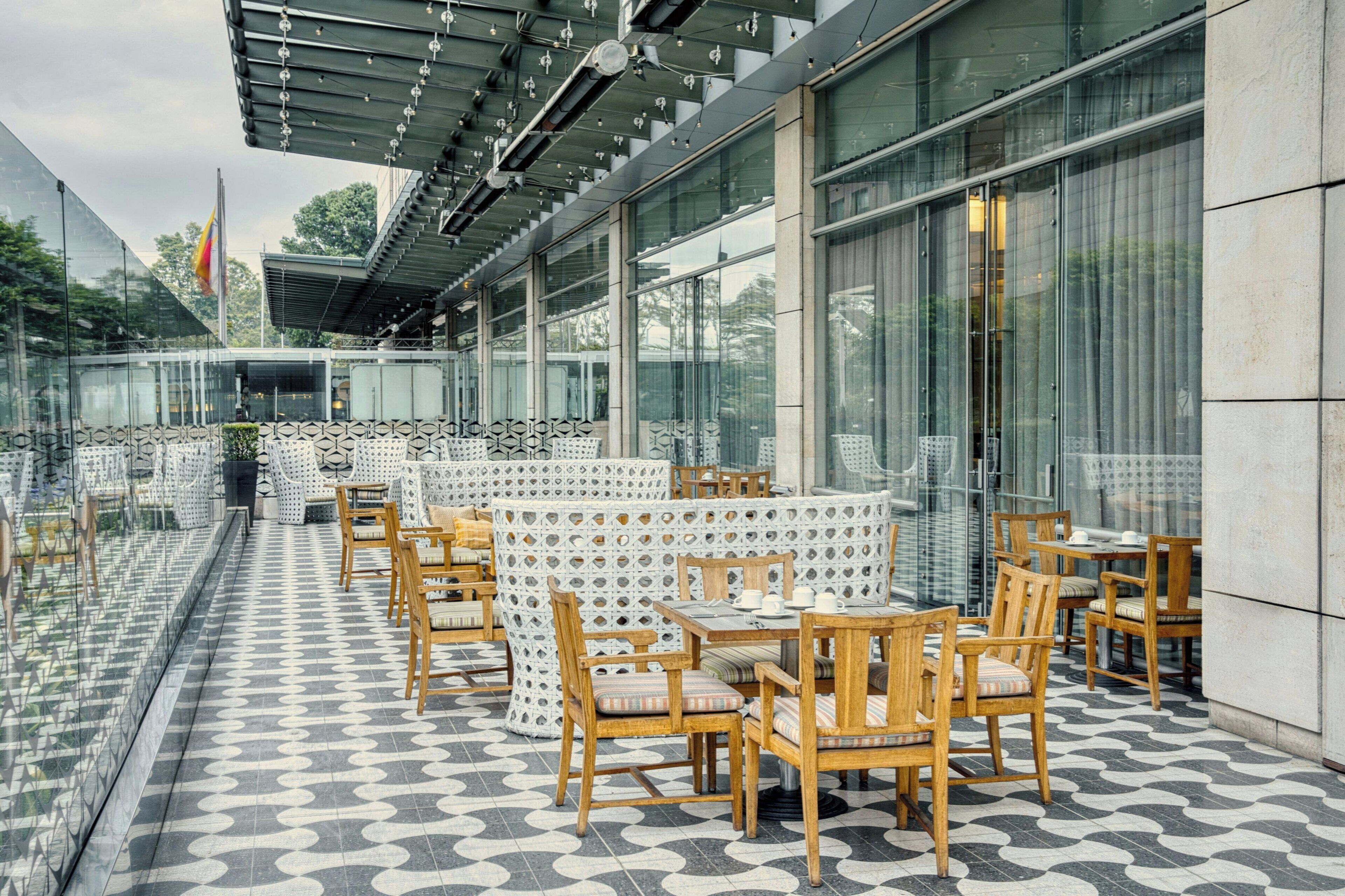 An outdoor patio area with tables and chairs, large windows, and a patterned floor.