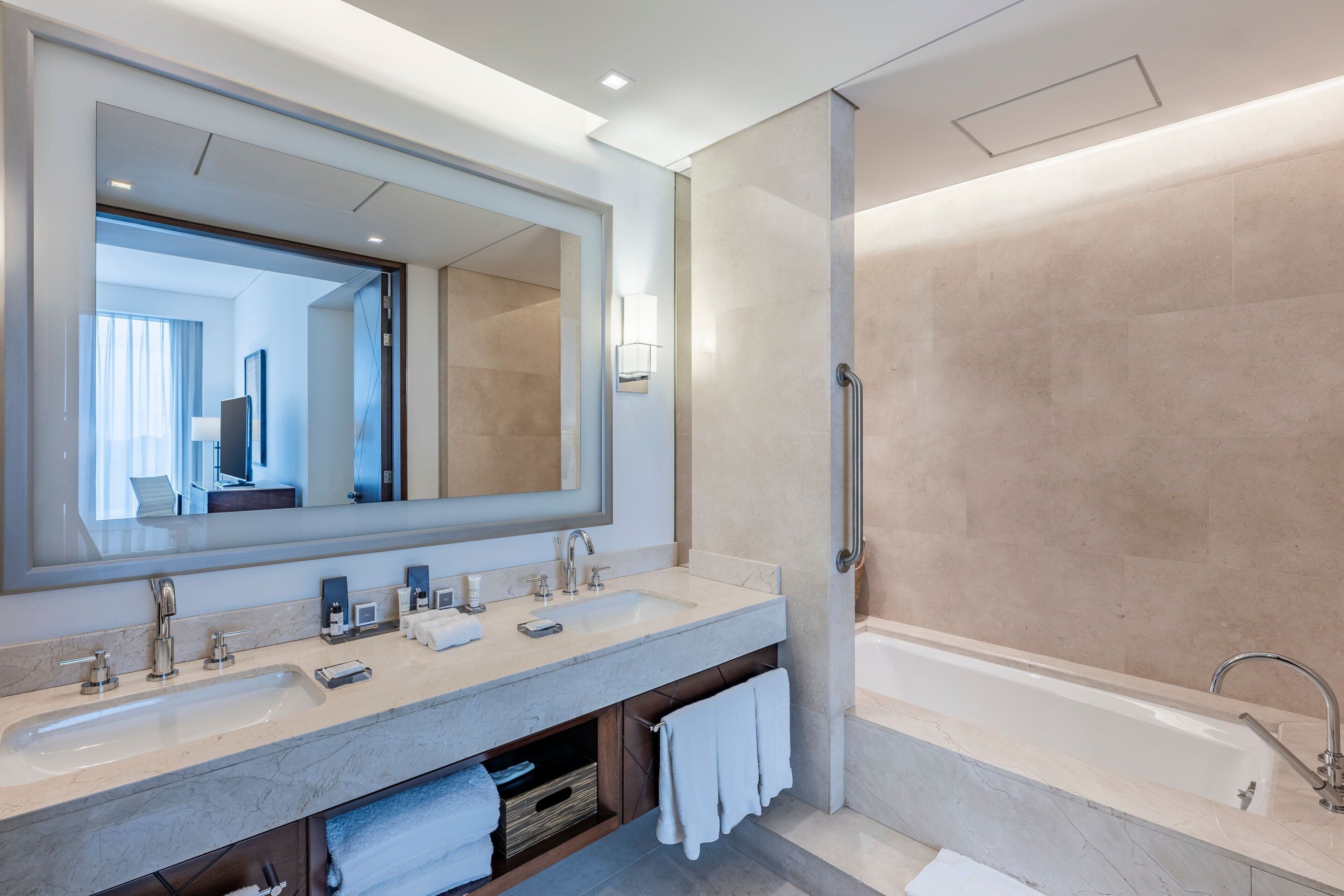 Un baño moderno con dos lavamanos, un espejo grande, una bañera y un perchero para toallas.