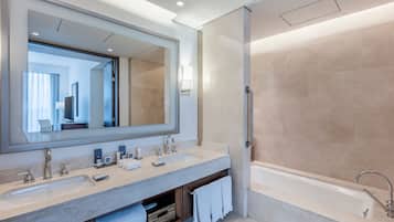 A modern bathroom with two sinks, a large mirror, a bathtub, and a towel rack.