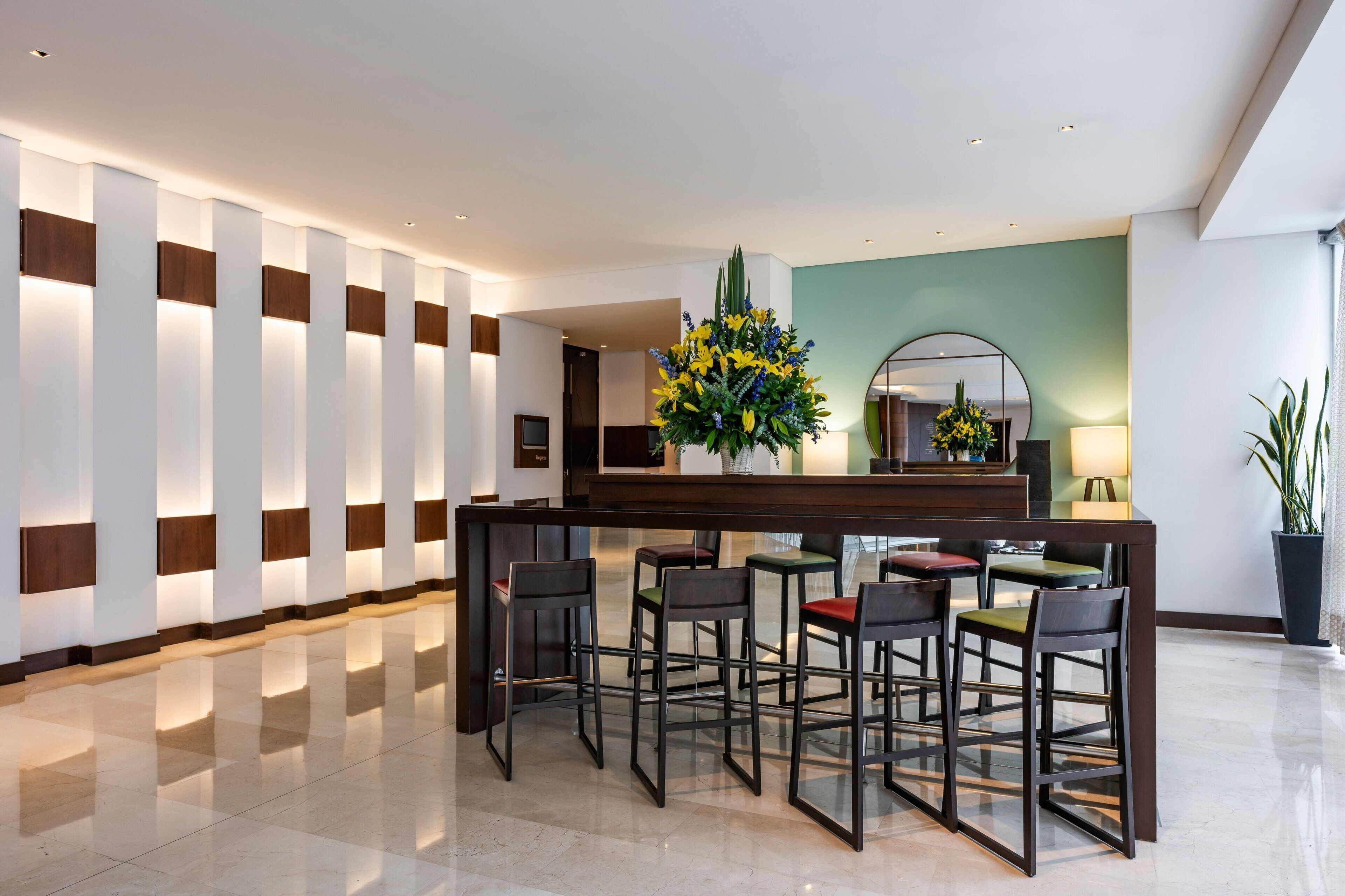 Un hall d’entrée moderne avec un comptoir d’accueil, des tabourets de bar et un grand miroir.