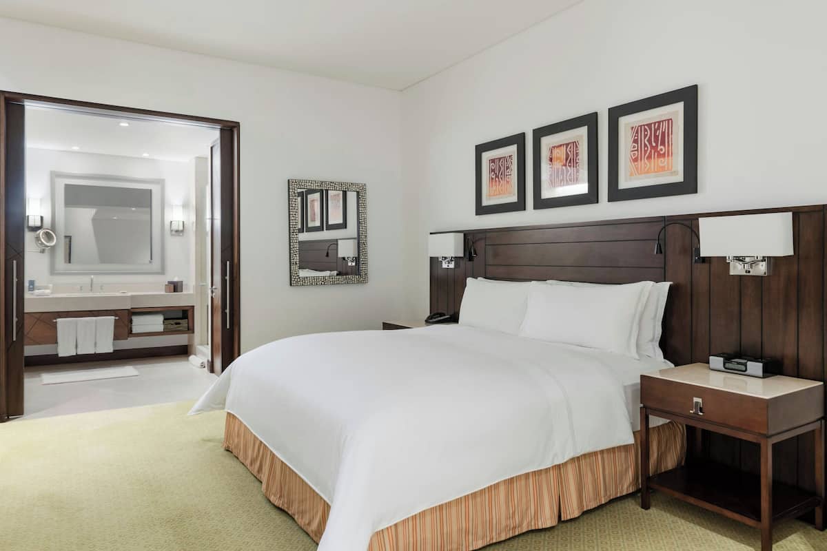 A hotel room with a large bed, a bedside table, a nightstand, a mirror, and a framed artwork on the wall.