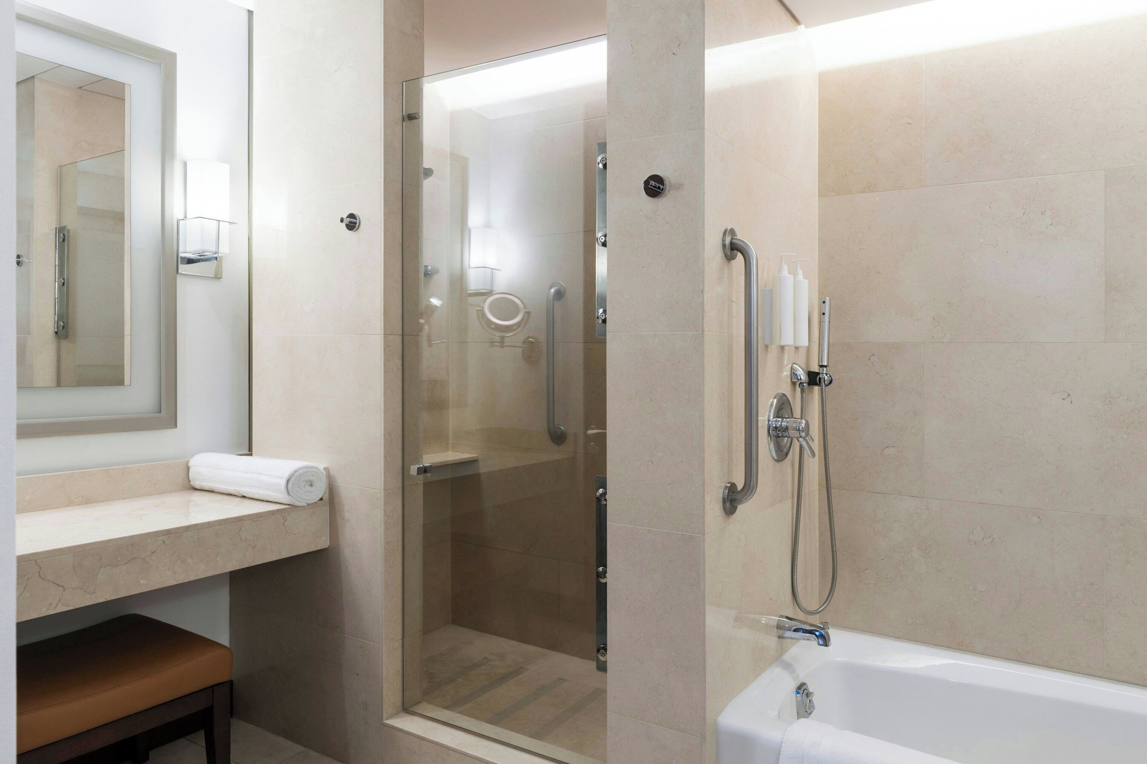 Ein modernes Badezimmer mit einer Duschkabine, einer Badewanne, einem Waschtisch mit Spiegel und einer Sitzbank.