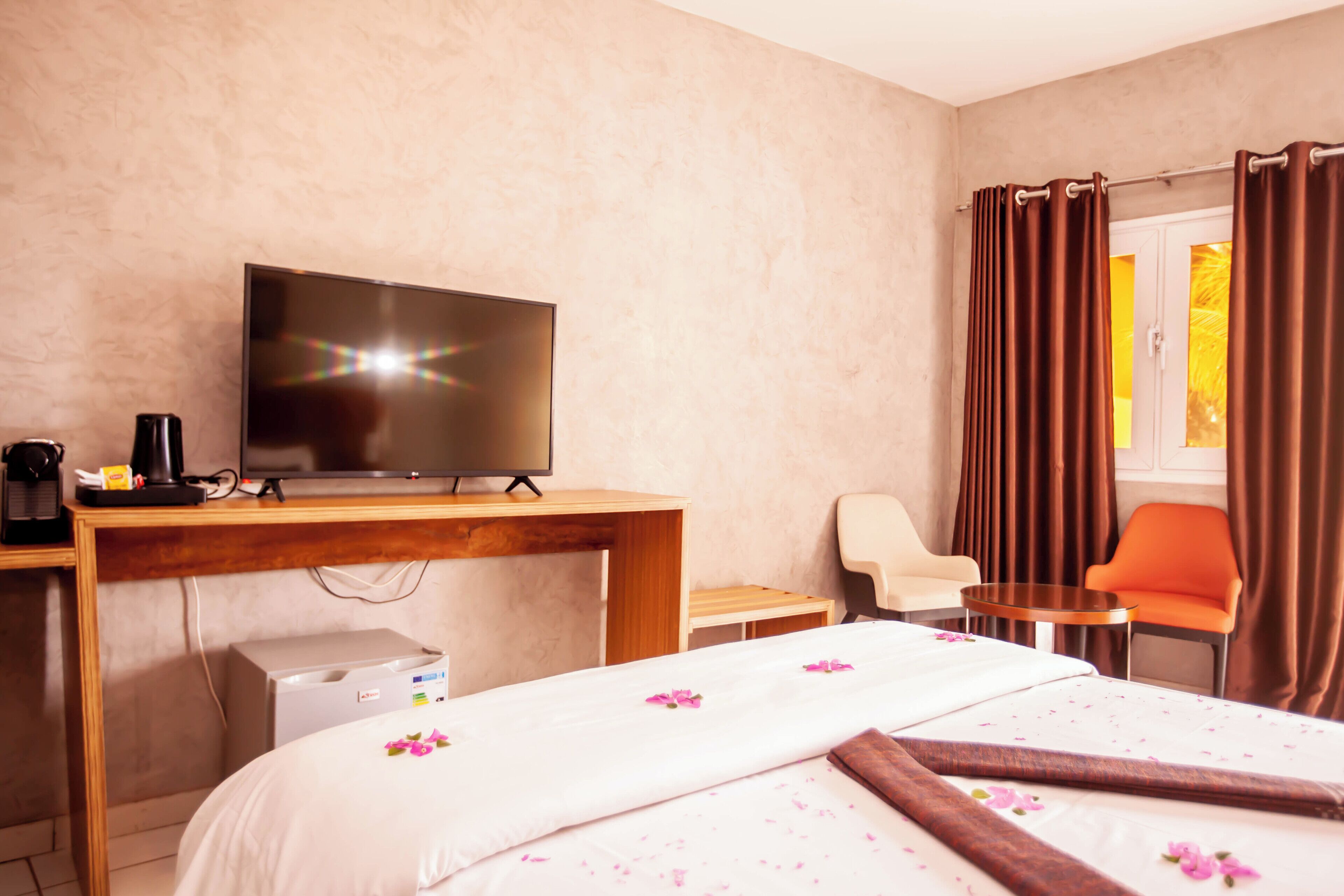 A hotel room with a bed, a TV, a desk, a chair, and a window with curtains.