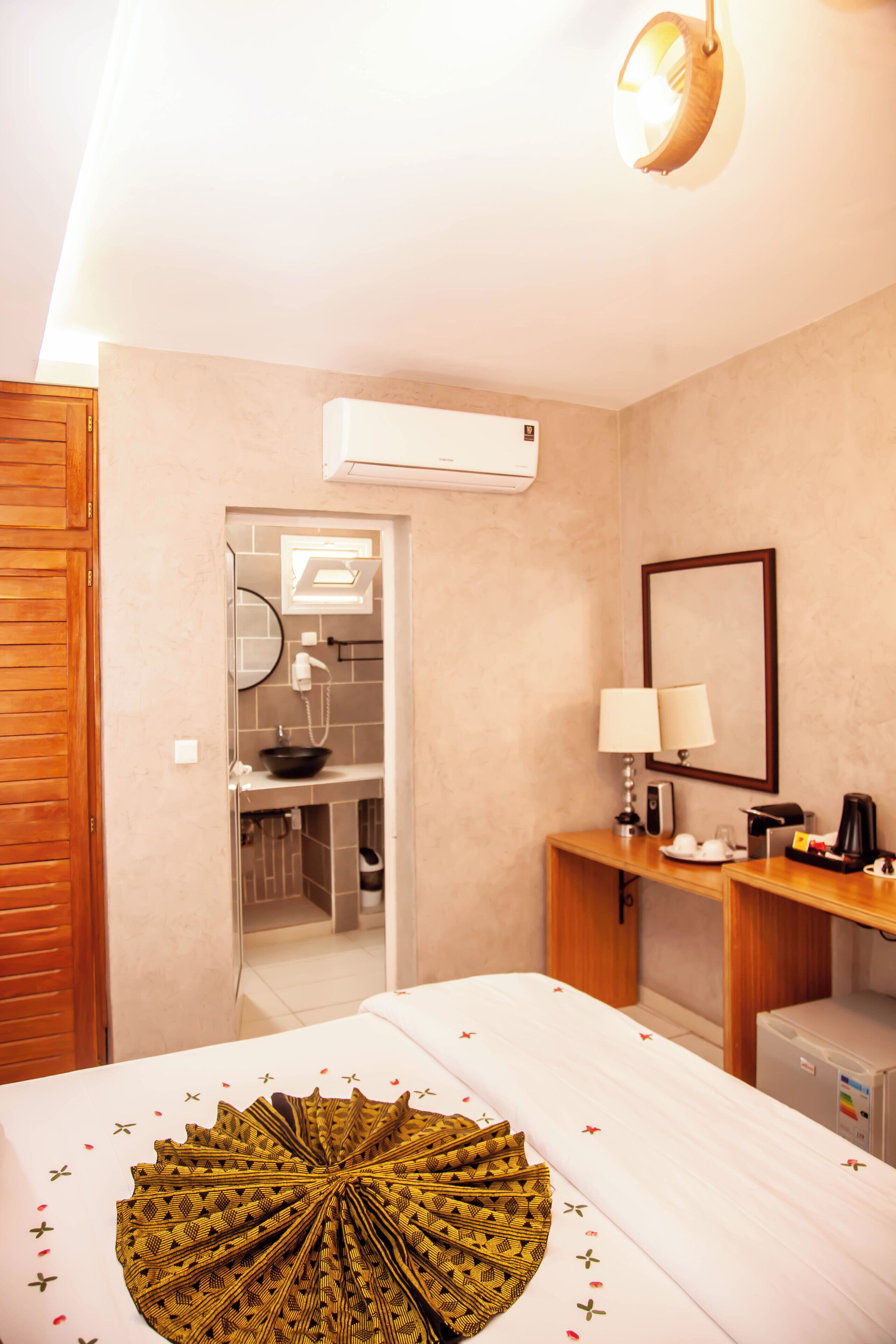A hotel room with a bed, a desk, a mirror, a sink, and an air conditioning unit.