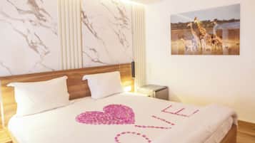 Cama bem arrumada com um edredom branco e uma decoração em forma de coração rosa com a palavra 'LOVE'.