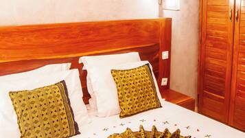 A hotel room with a wooden headboard, a large bed with patterned pillows, a decorative fan, and a wardrobe.