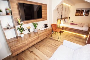 Un dormitorio moderno con un televisor grande montado en una pared de madera, una cama con cabecera y una zona de estar con una silla y un sofá.