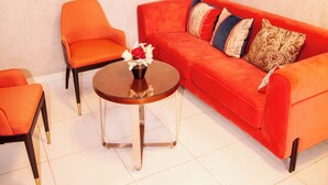 A modern living room with a red sofa, orange armchair, and a small round table with a vase of flowers. - Hotel Flamboyants (Mbour)