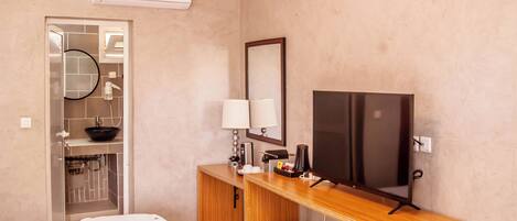 A hotel room with a bed, a desk with a television, a small refrigerator, and a mirror.