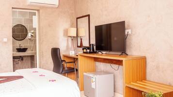 A hotel room with a bed, desk, chair, television, and a small refrigerator.