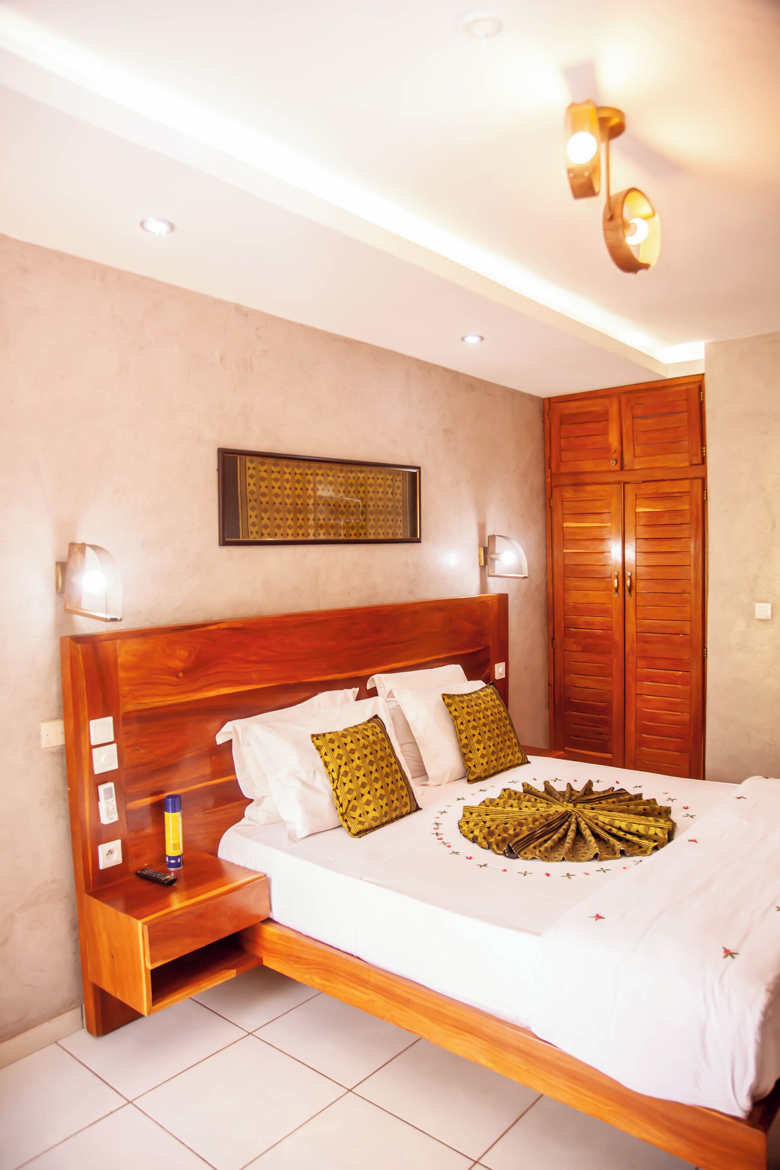 Un dormitorio con una cama de madera, lámparas de noche, una mesita de noche, un armario y un elemento decorativo en la pared.