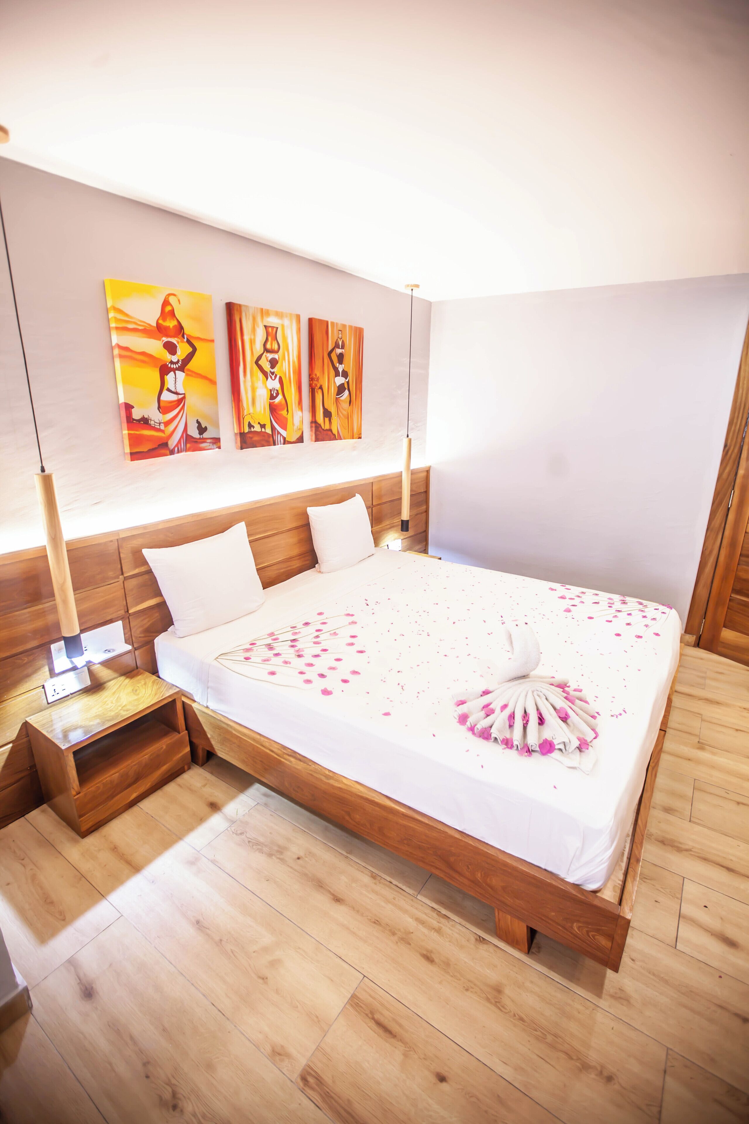 Een slaapkamer met een houten bed, witte beddengoed en drie schilderijen aan de muur.