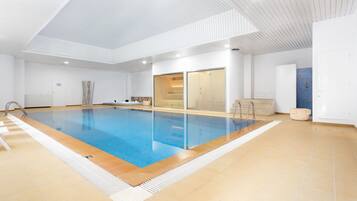 Ein geräumiges Hallenbad mit klaren Glaswänden, gefliestem Boden und modernem Deckenbau.